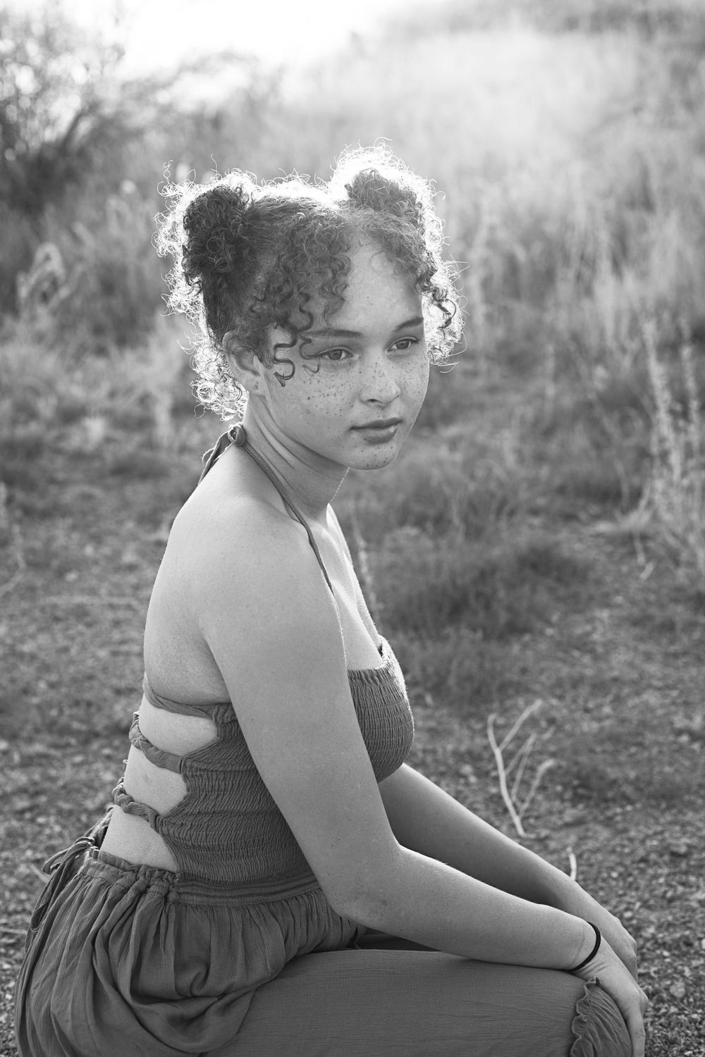 Black and white portrait of someone in a dress sitting outdoors with curly hair.