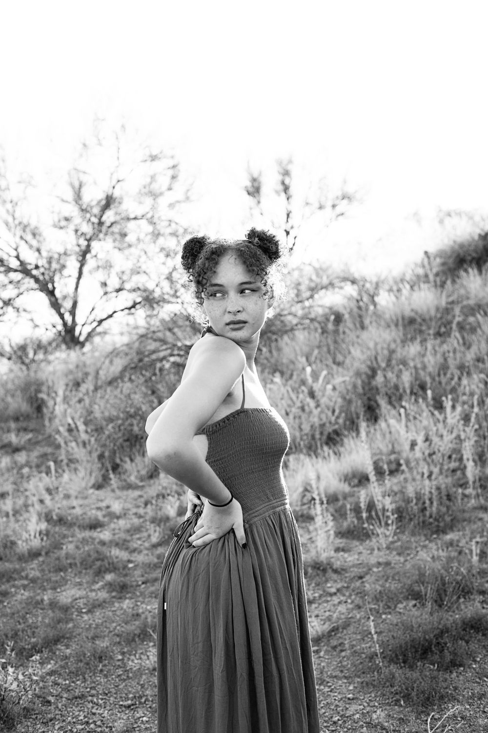 Black and white photo of someone in a flowing dress posing in desert terrain.