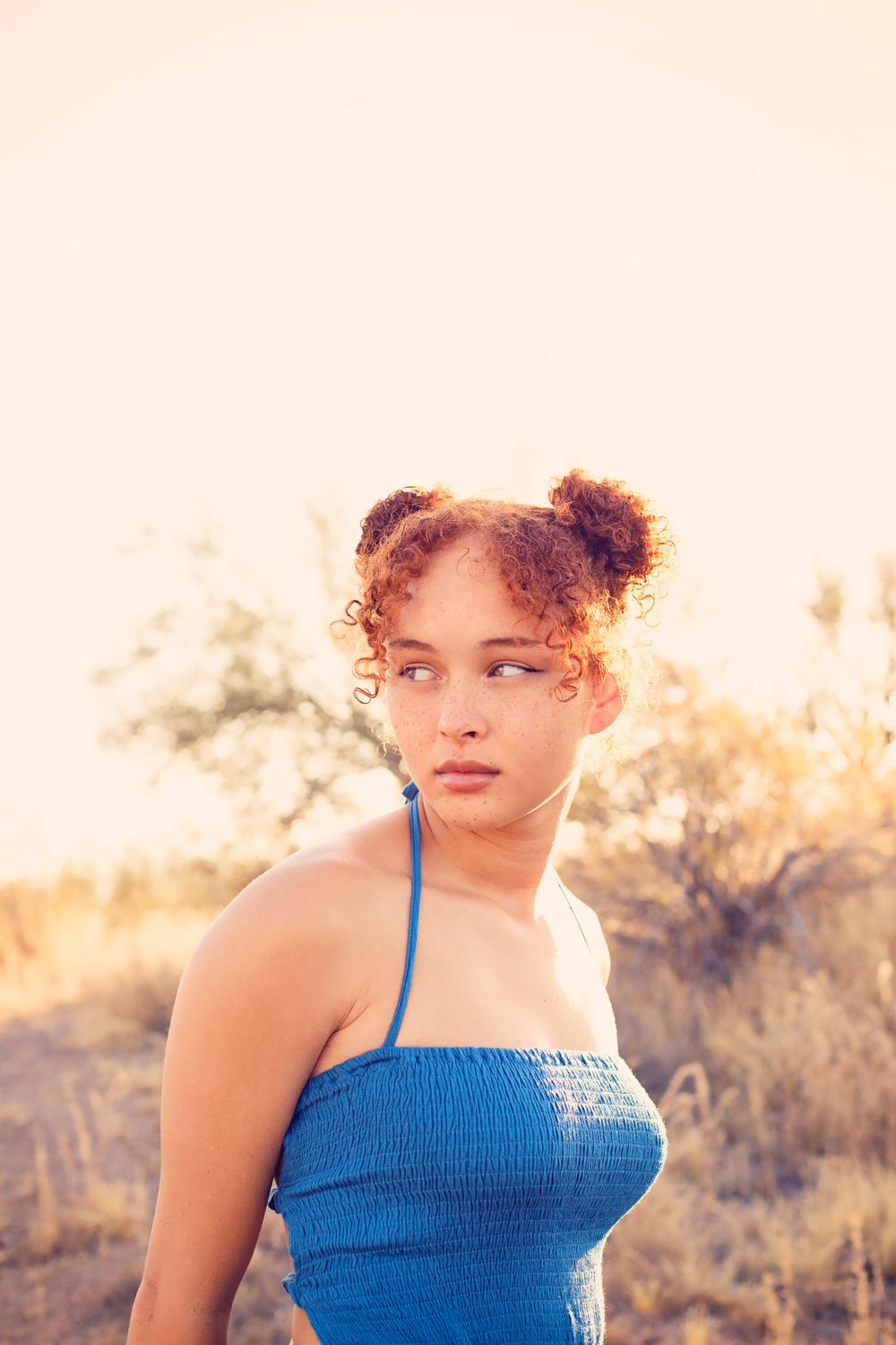 Person wearing a blue smocked top poses against a warm desert sunset backdrop.