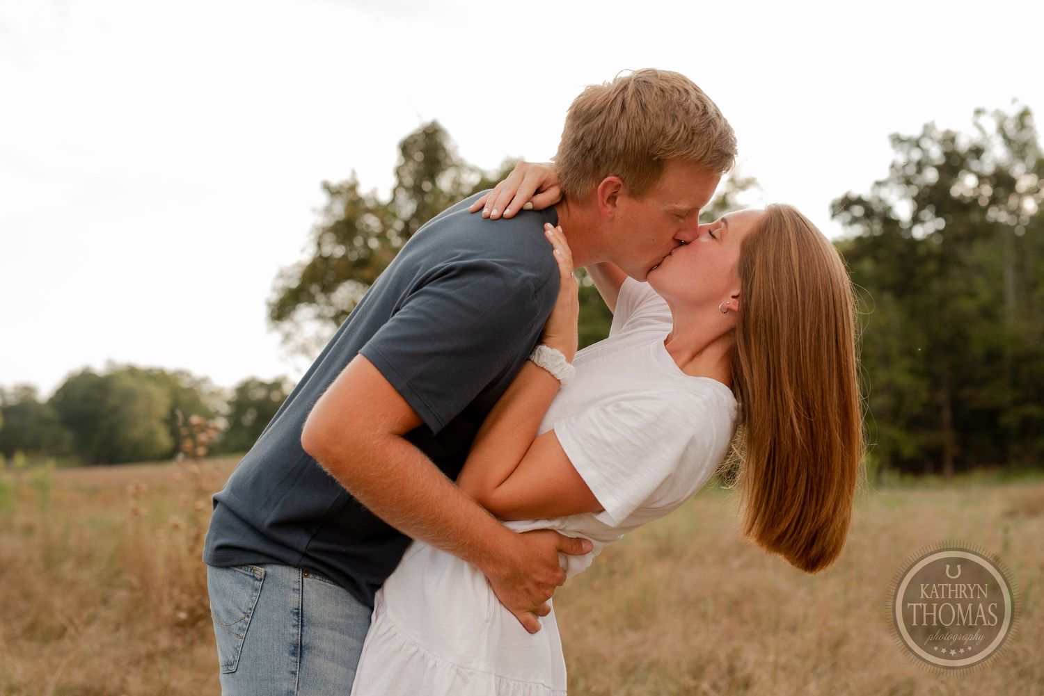 Romantic couple sharing a tender kiss in a rustic field at sunset.