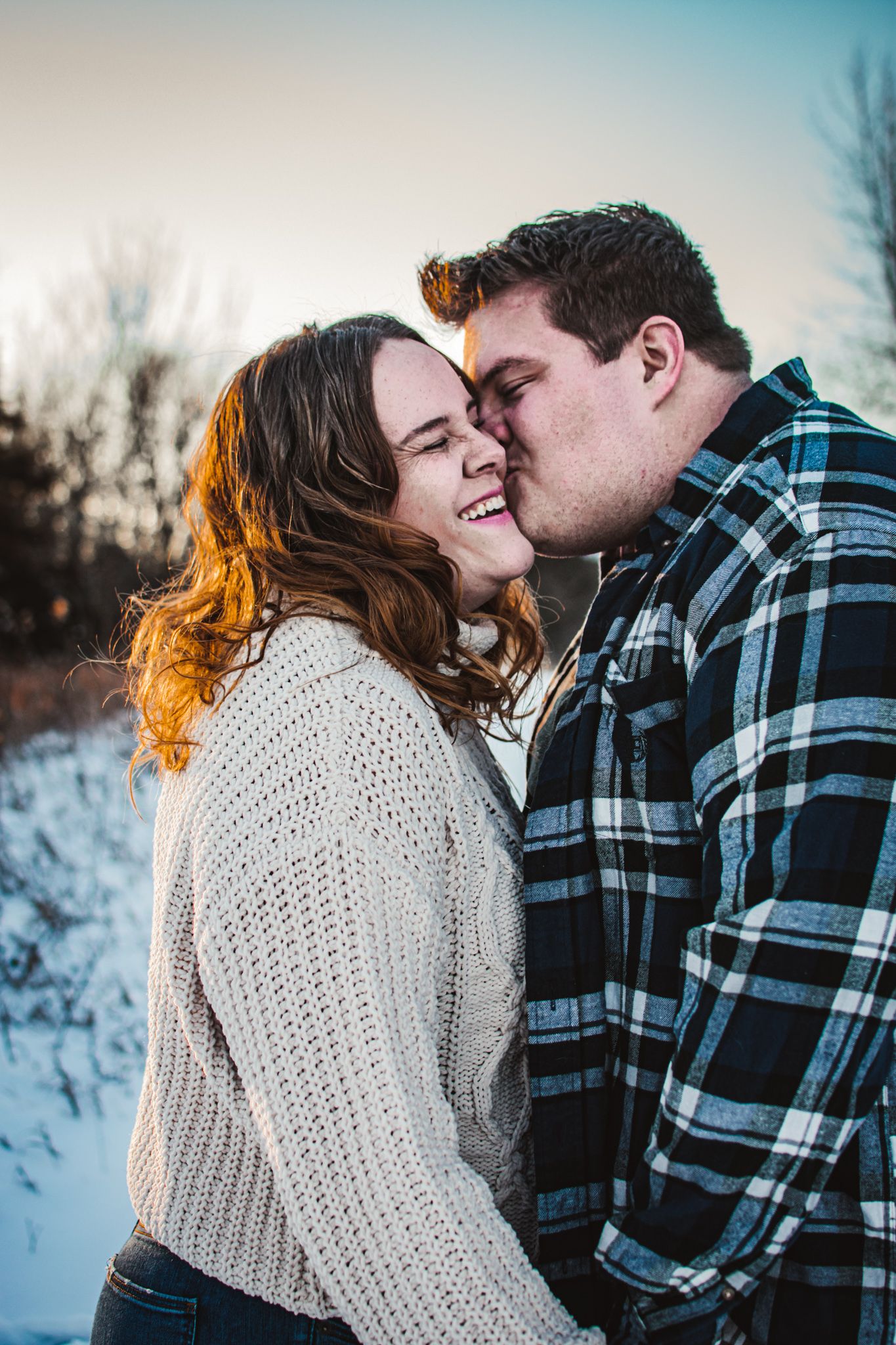 A tender winter moment between a couple in plaid and knit sweaters against a snowy backdrop.