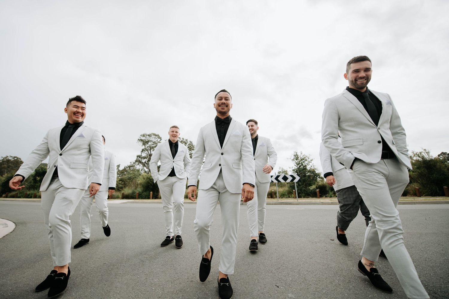Group of groomsmen in matching light grey suits walking together on a cloudy day.