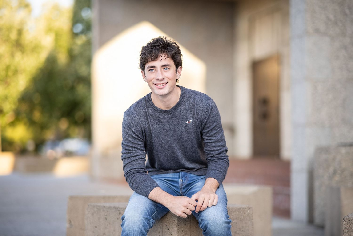 Minnesota high school senior boy with dark hair and dark grey crewneck seated on granite block.
