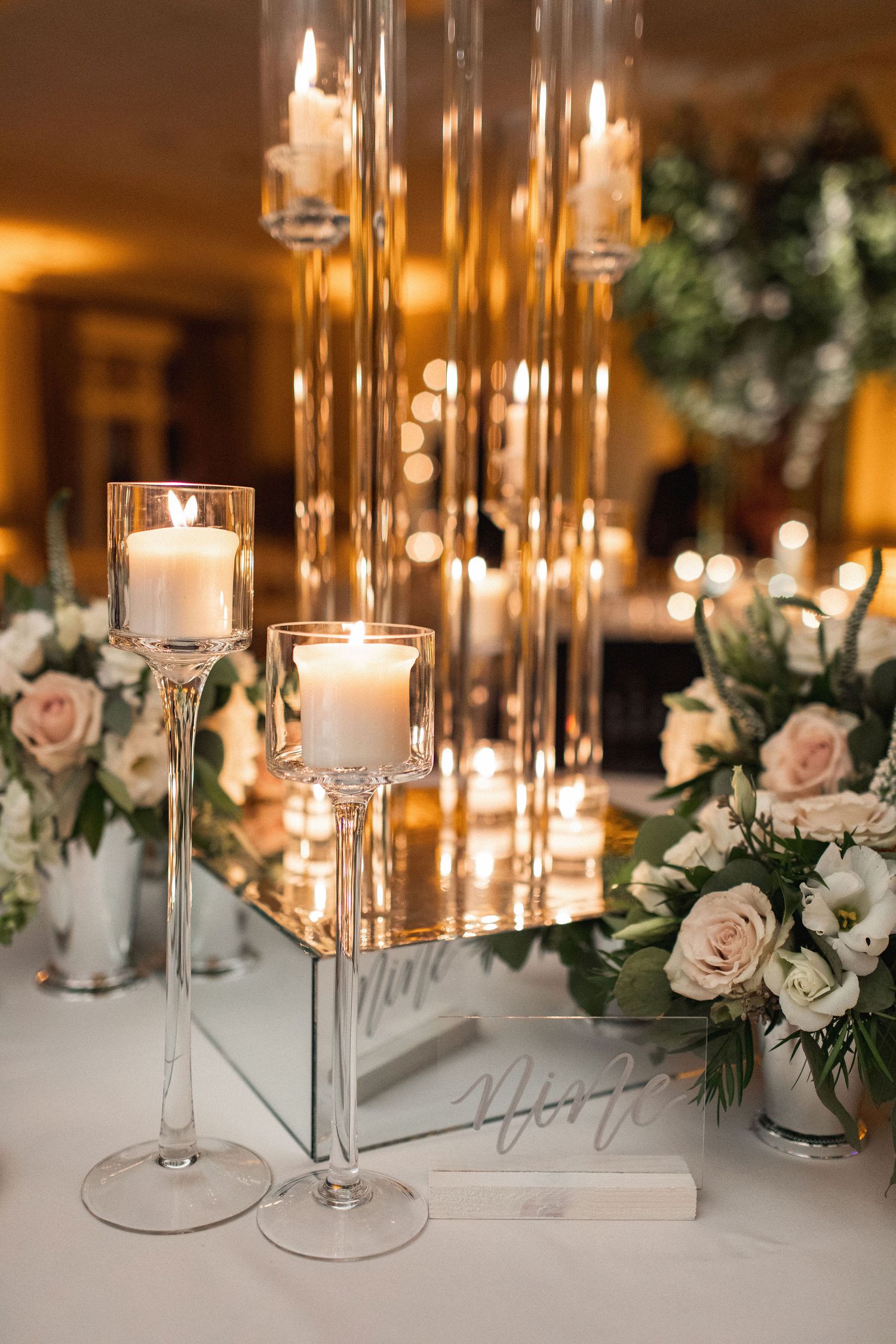 Romantic wedding centerpiece with tall glass candleholders and pale pink floral arrangements.