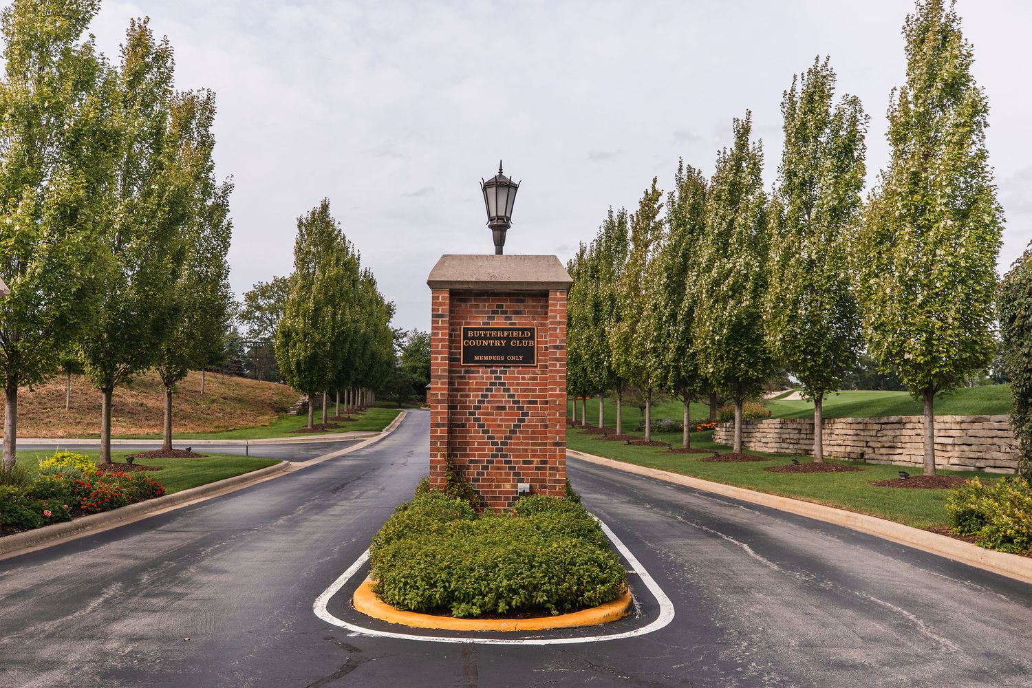 Brick entrance pillar with lantern surrounded by poplar trees and curved road.