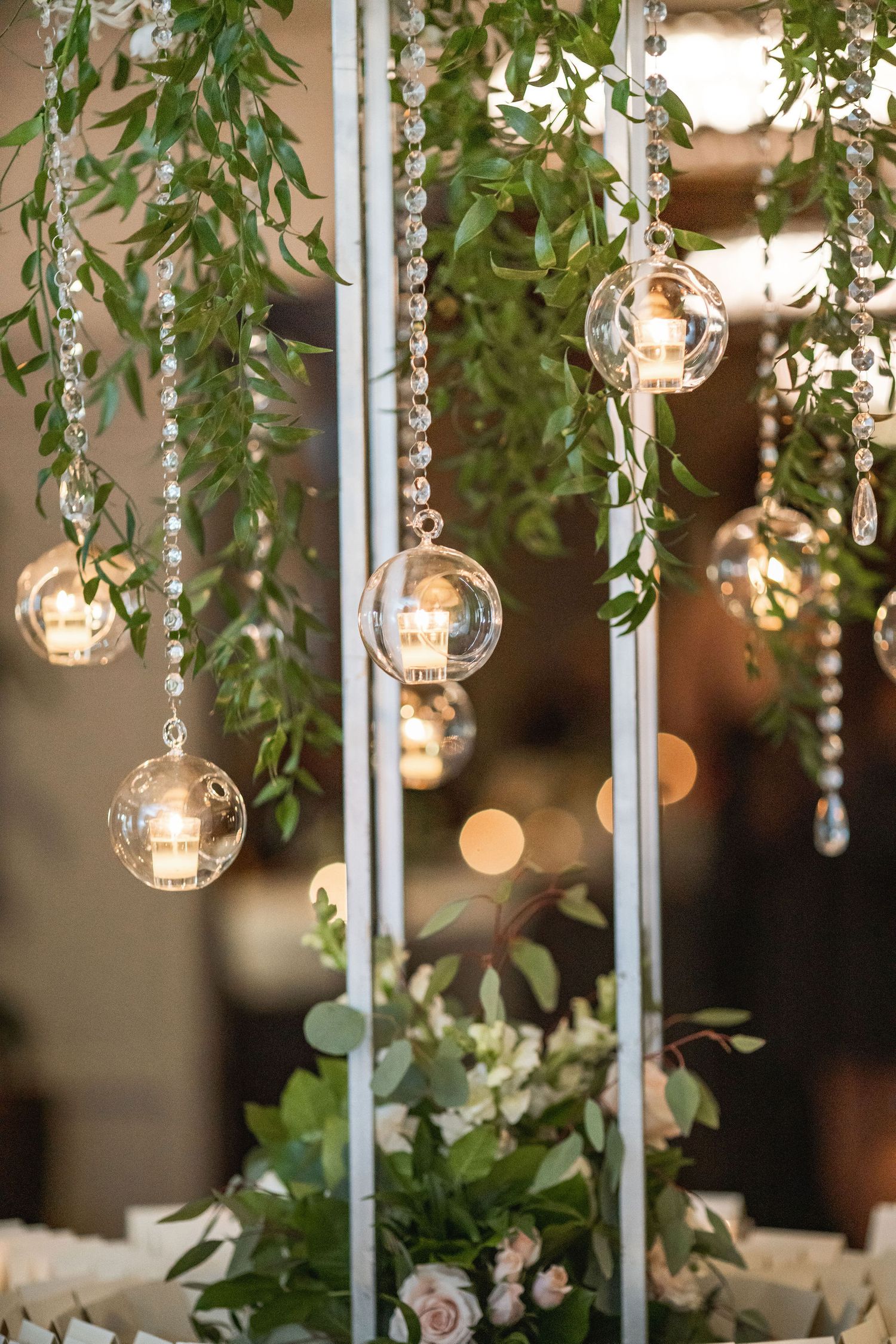 Hanging glass orb lights with crystal strands and greenery create ethereal wedding decor.