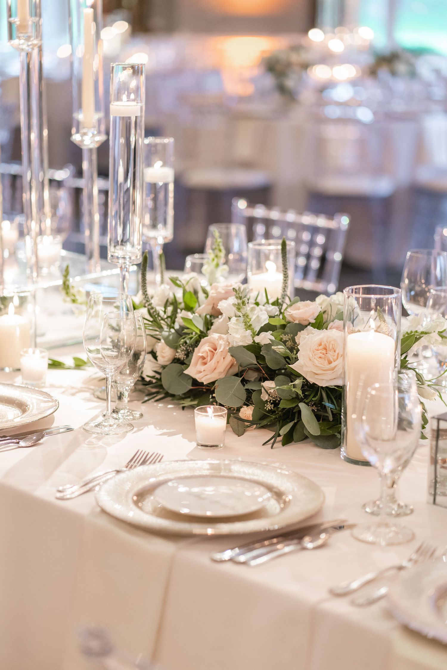 Elegant wedding table setting with blush roses, crystal glassware and white linens.