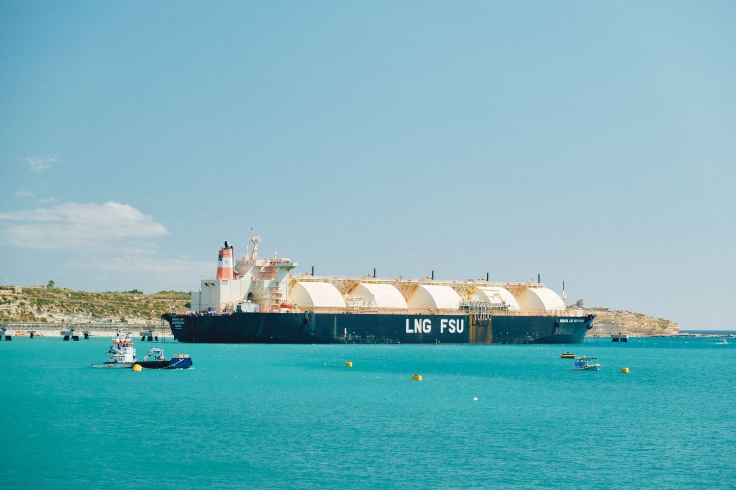 Large cargo ship anchored in bright turquoise Mediterranean waters.
