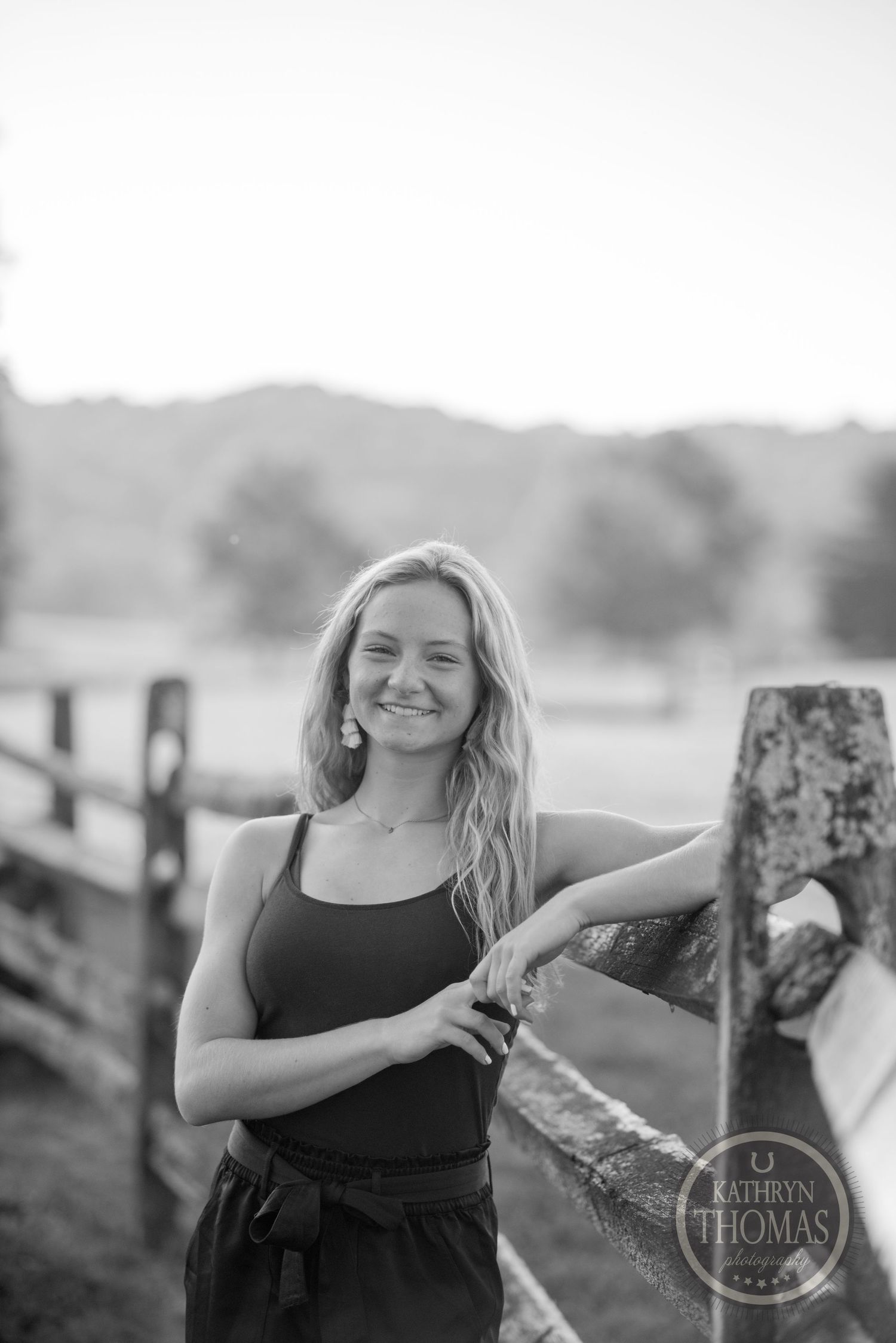 Black and white portrait by rustic wooden fence with countryside backdrop.
