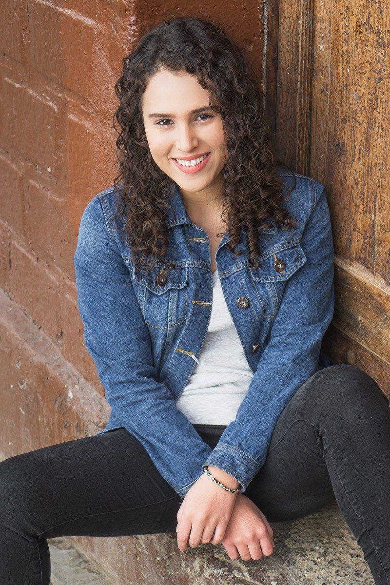 Portrait of young woman with curly hair leaning against brick wall