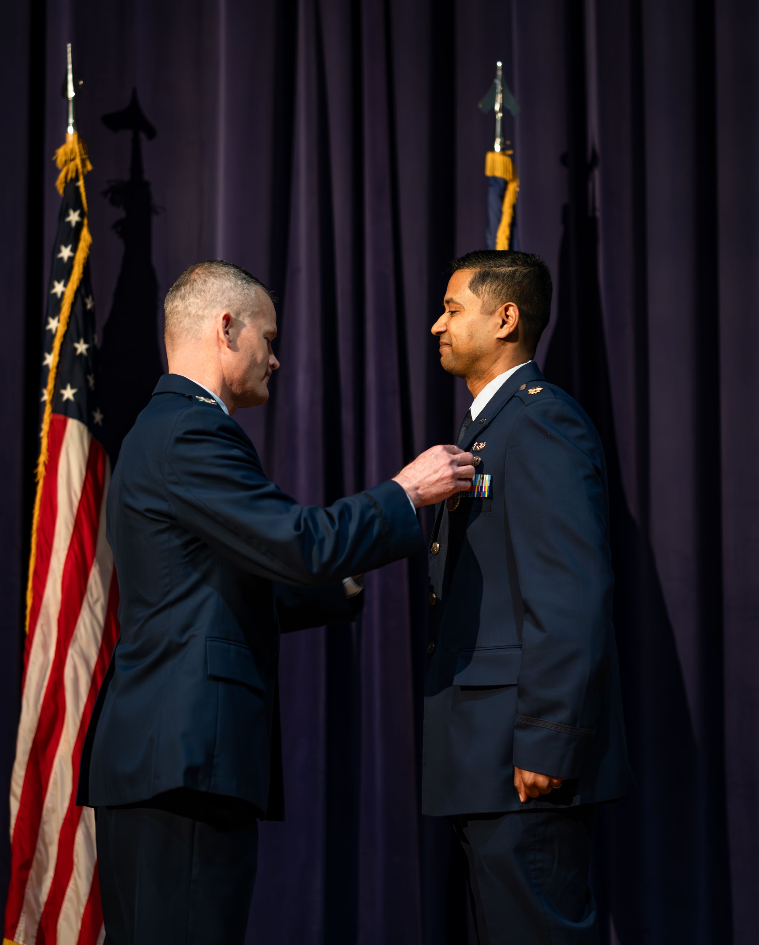 Military service members stand in formation during a formal ceremony with American flags in the background.