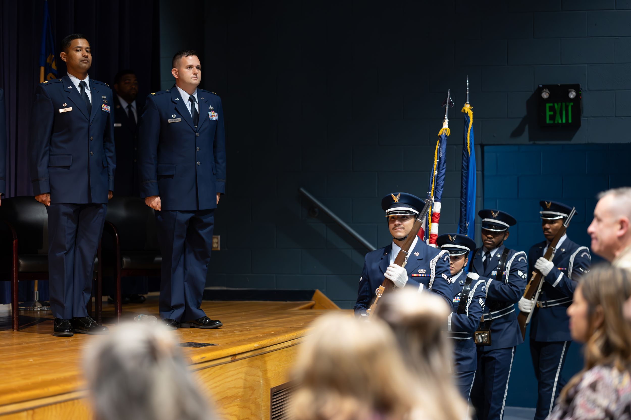 Honor guard members perform rifle drills during a military ceremony with audience members visible.