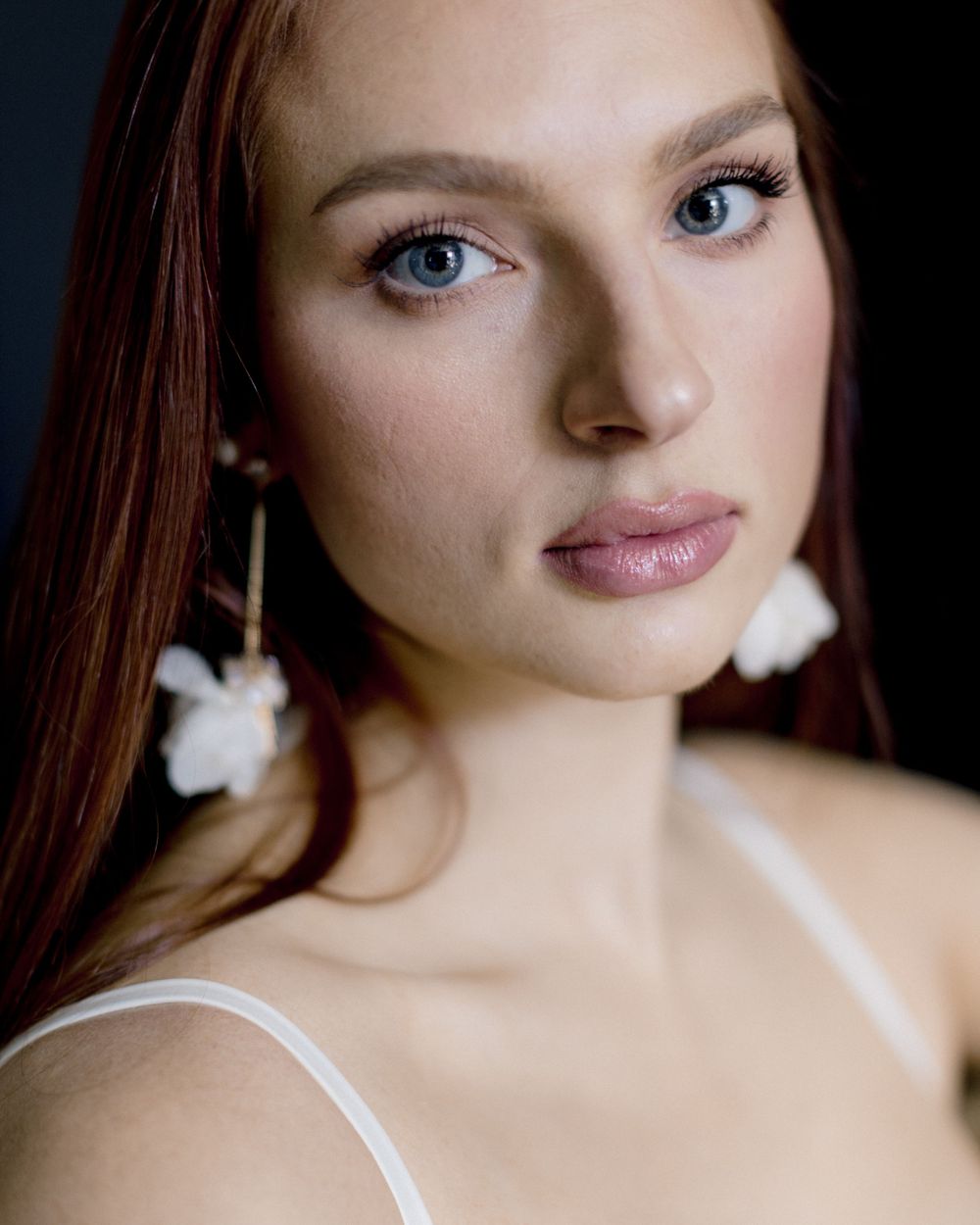 Portrait with white floral earrings and natural makeup against dark background.