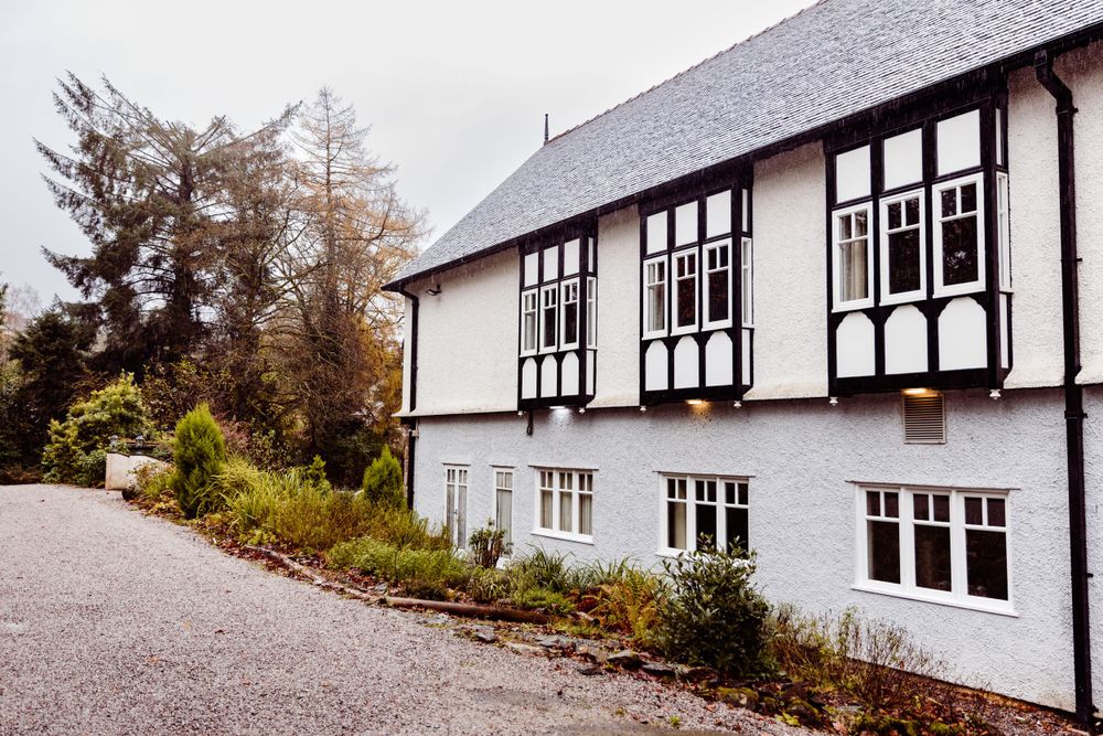 Traditional white Tudor-style house with black trim and gravel driveway.