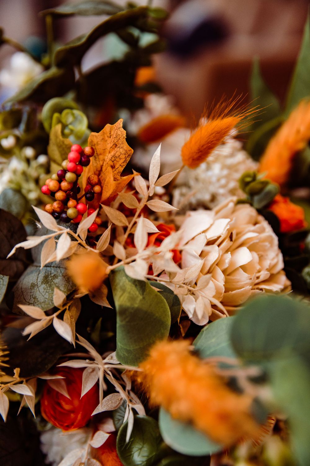 Detailed macro shot of a romantic wedding bouquet with cream flowers, orange accents, and green foliage.