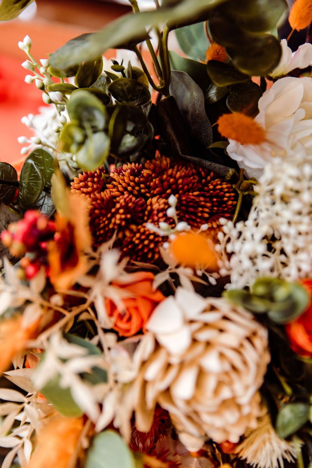 Close-up of a vibrant autumn-toned wedding bouquet with orange and white flowers and berries.
