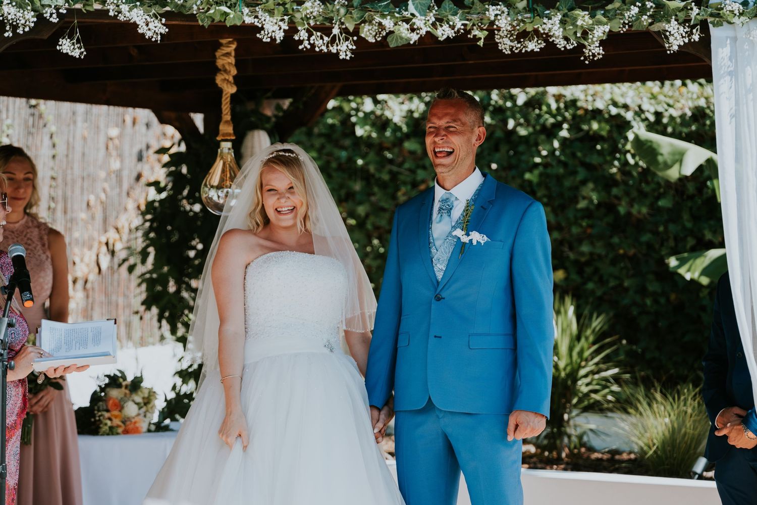A joyful wedding ceremony moment under an arbor adorned with white flowers.