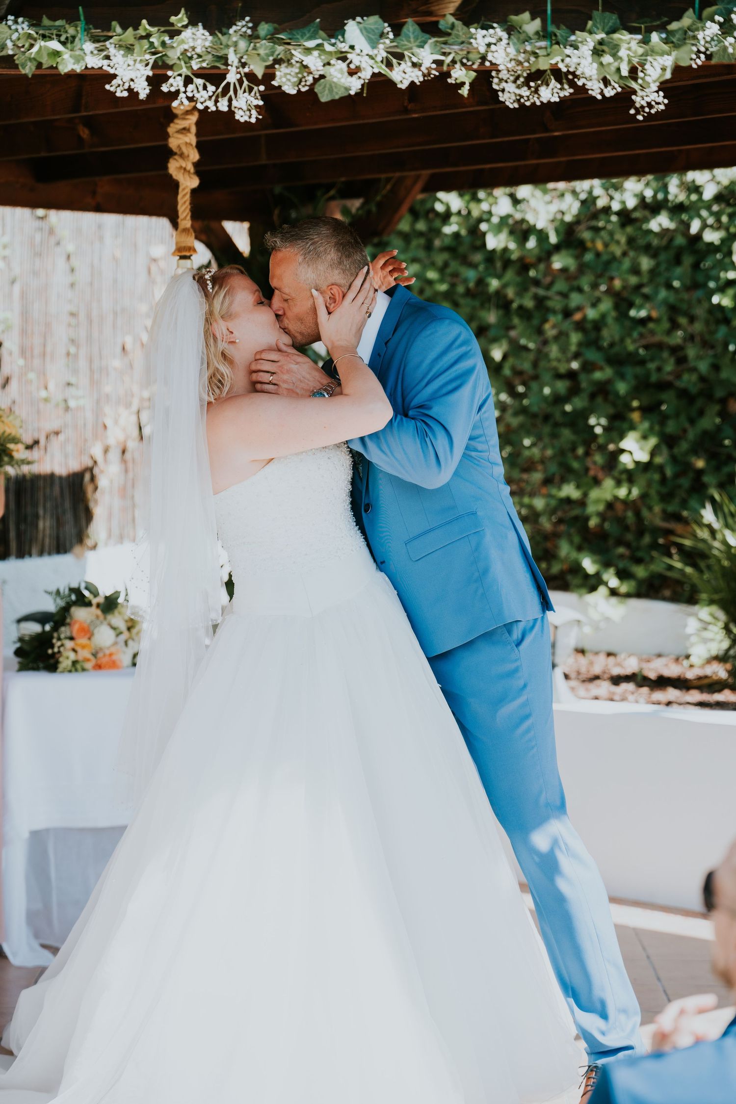 A romantic kiss shared under a floral-decorated wedding arbor.