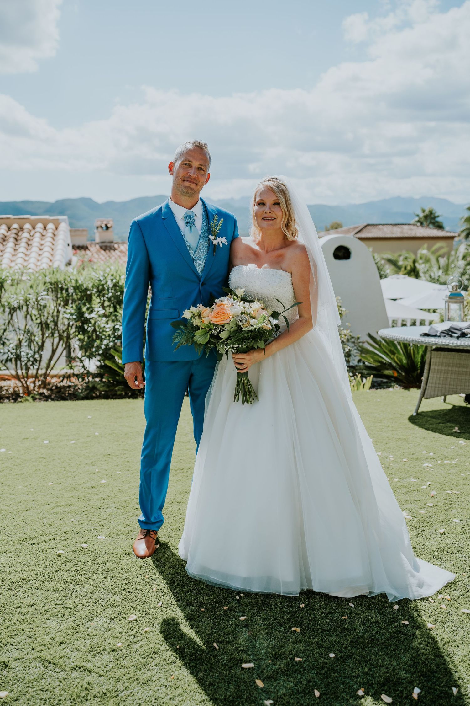 A sunny outdoor wedding portrait with mountains and blue sky in the background.