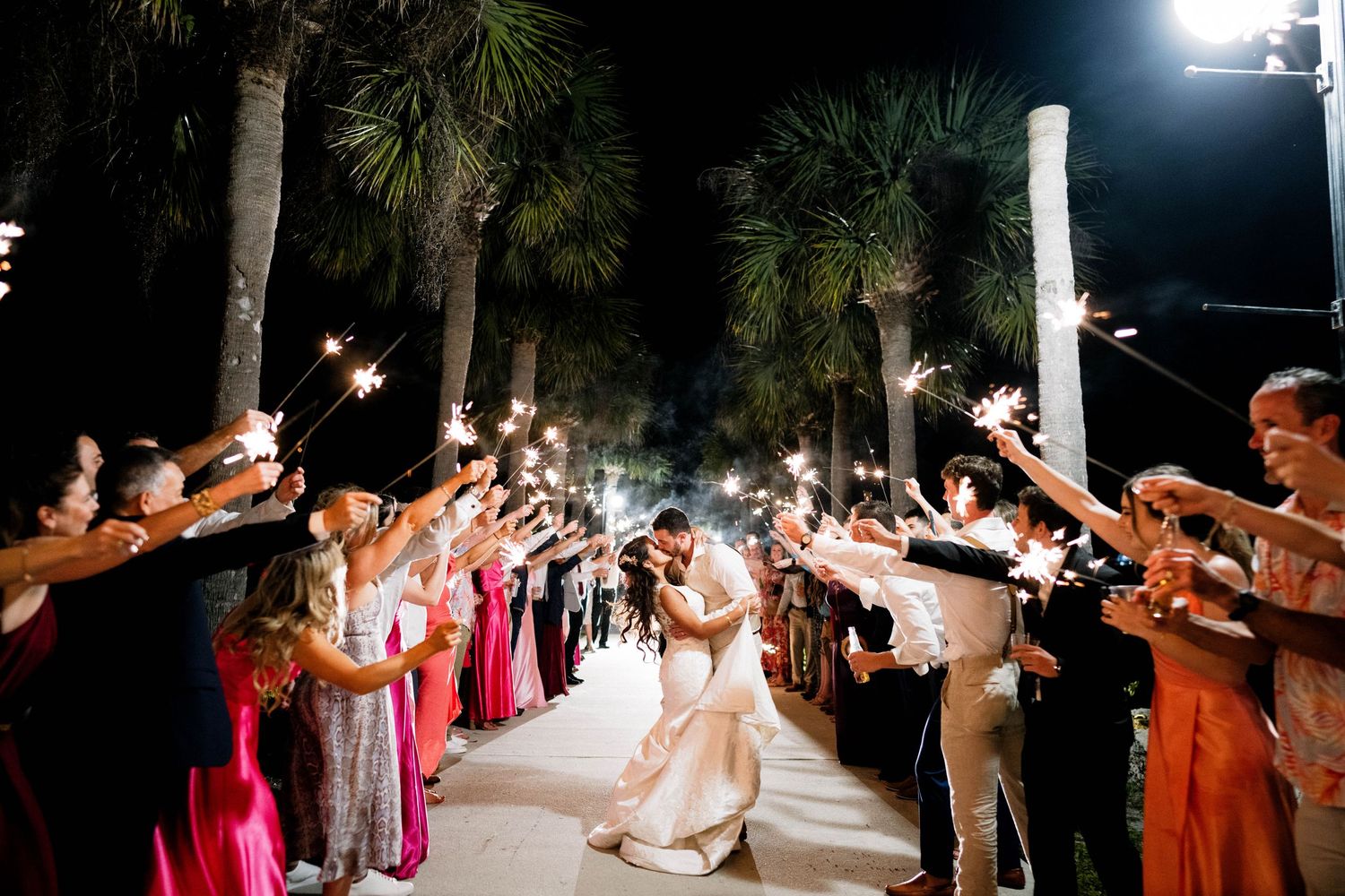 Newlyweds exit through sparkler tunnel lined with guests in formal attire.