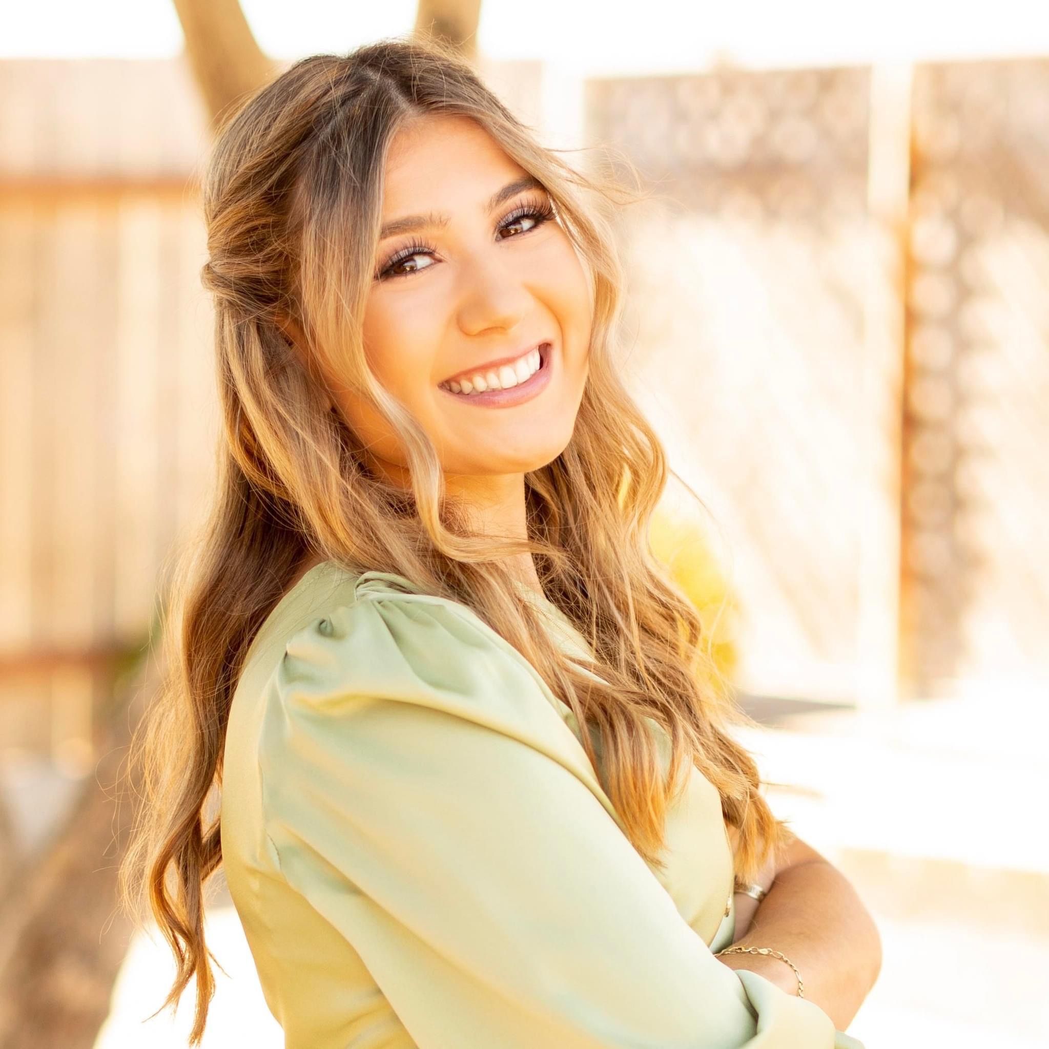 Portrait of young woman in yellow top smiling in warm sunlight.