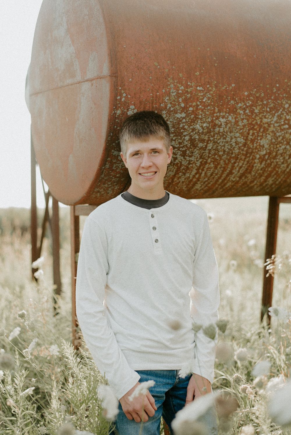 Person in white henley shirt standing in front of rustic metal tank in rural field.