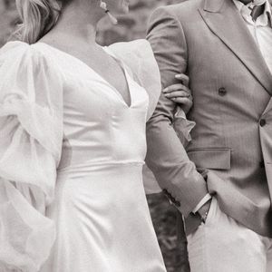 Cropped wedding photo showing a white gown with puff sleeves next to a tan suit jacket.