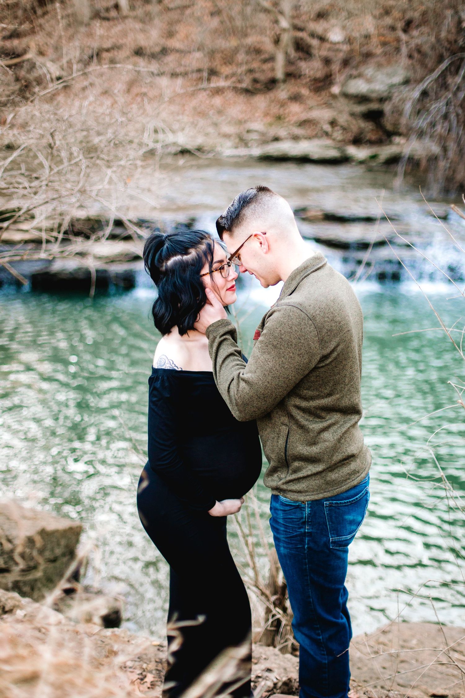 pregnant woman and husband pose for newborn photos near river in Lee's Summit, Missouri