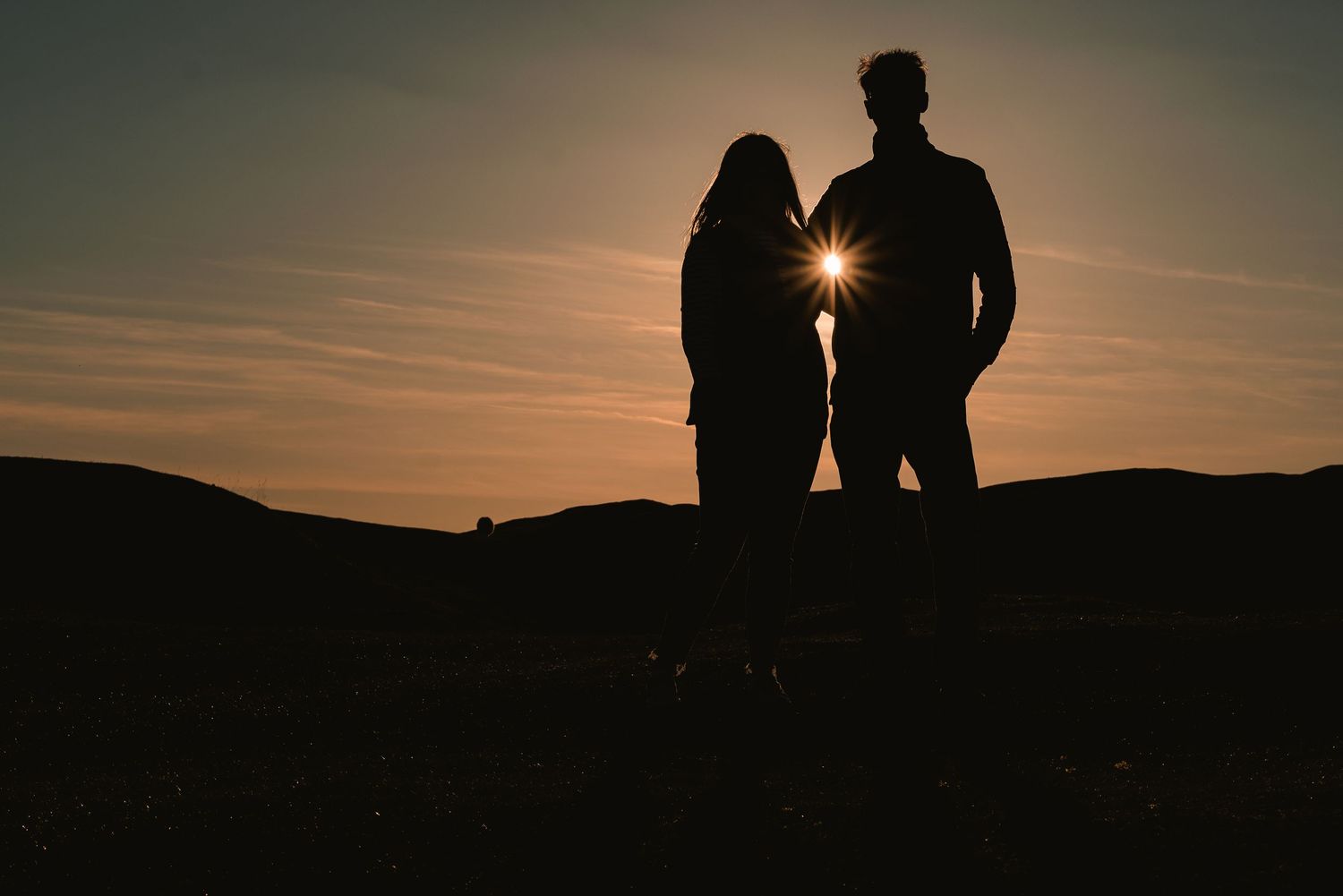 A silhouette of a young couple, with the sun shining through a little gap of their arms. Countryside
