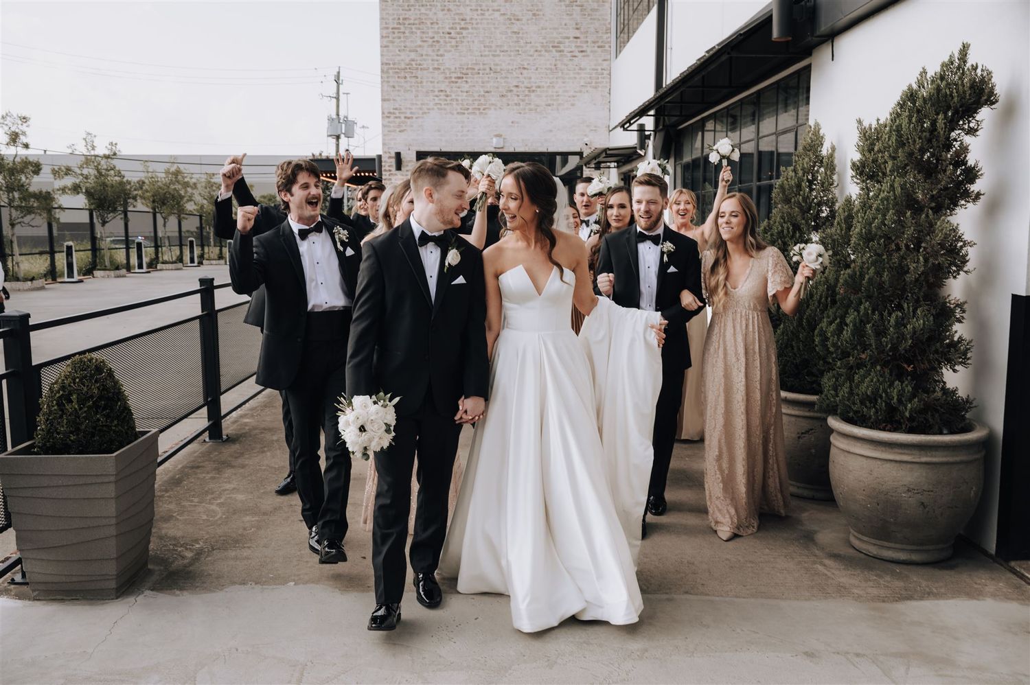 Wedding party walking together on outdoor terrace with bride in white gown.