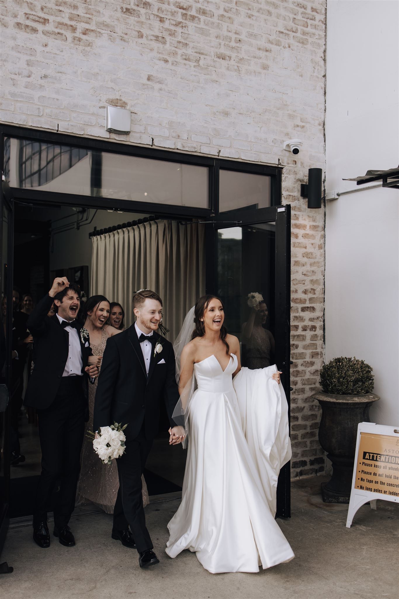 Wedding couple exiting modern venue with exposed brick walls.