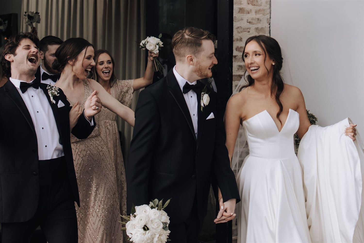 Wedding party sharing candid moment outside brick building.