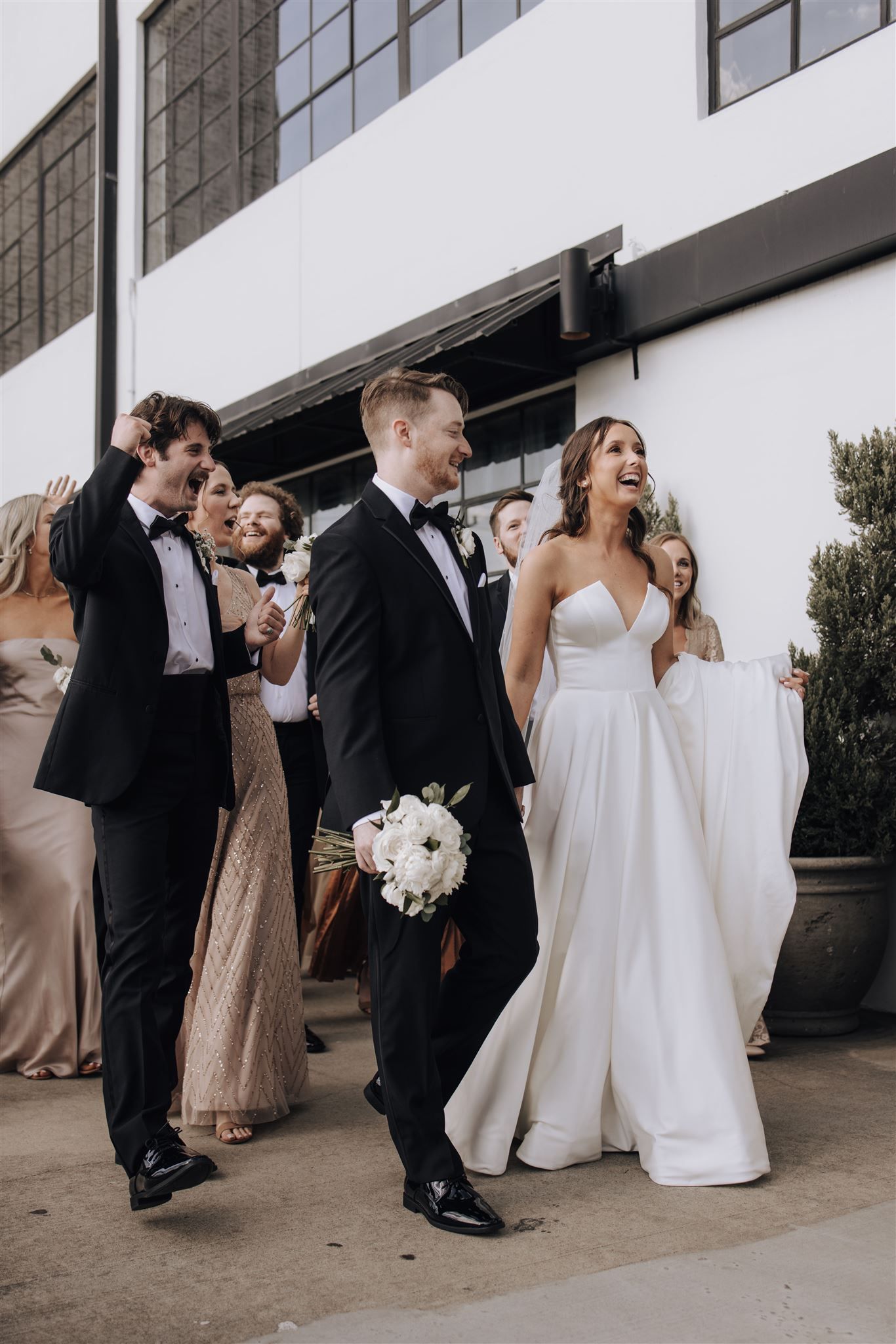 Wedding party walking together outside modern building with white walls.