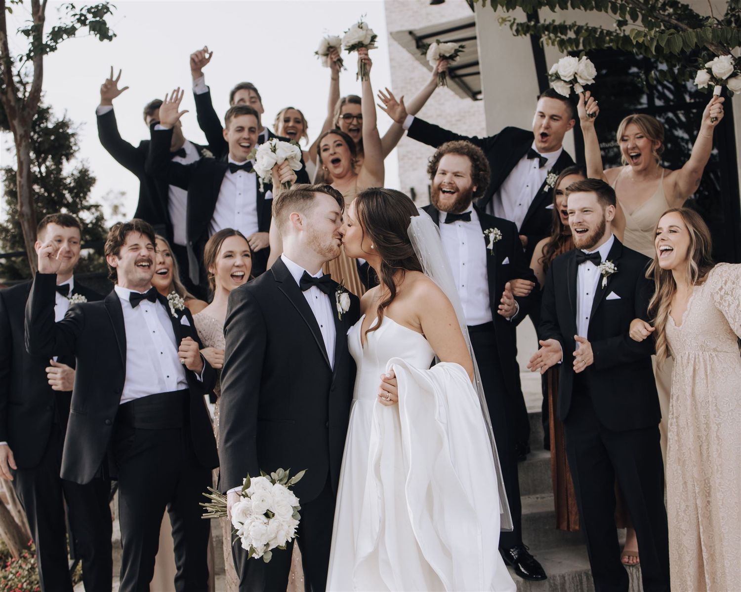 Wedding party celebrating with raised arms and champagne while standing outside.