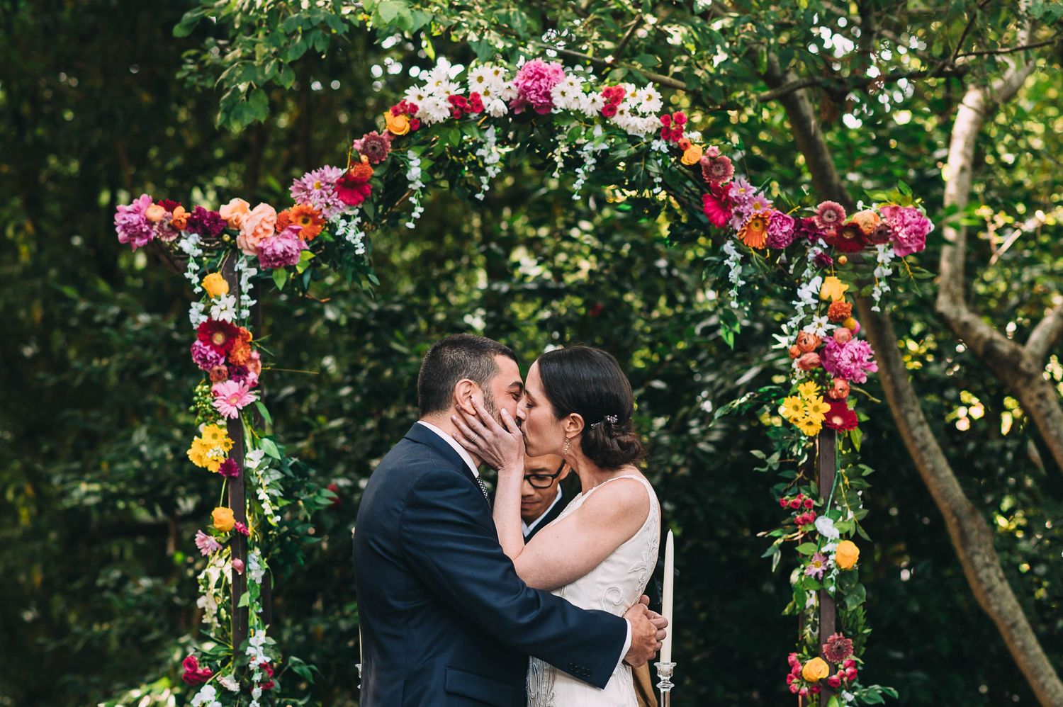 Wedding ceremony under a vibrant floral arch with pink and orange blooms in a garden setting.