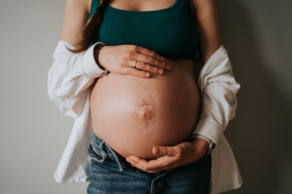 mama czule obejmuje ciążowy brzuszek - sesja domowa Kraków