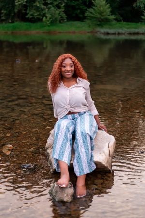 Person in flowing striped skirt standing barefoot on rocks in a serene lake setting.