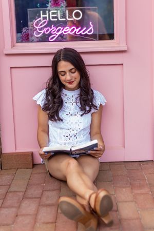 Reading scene with pink wall and neon 'Hello Gorgeous' sign in background.