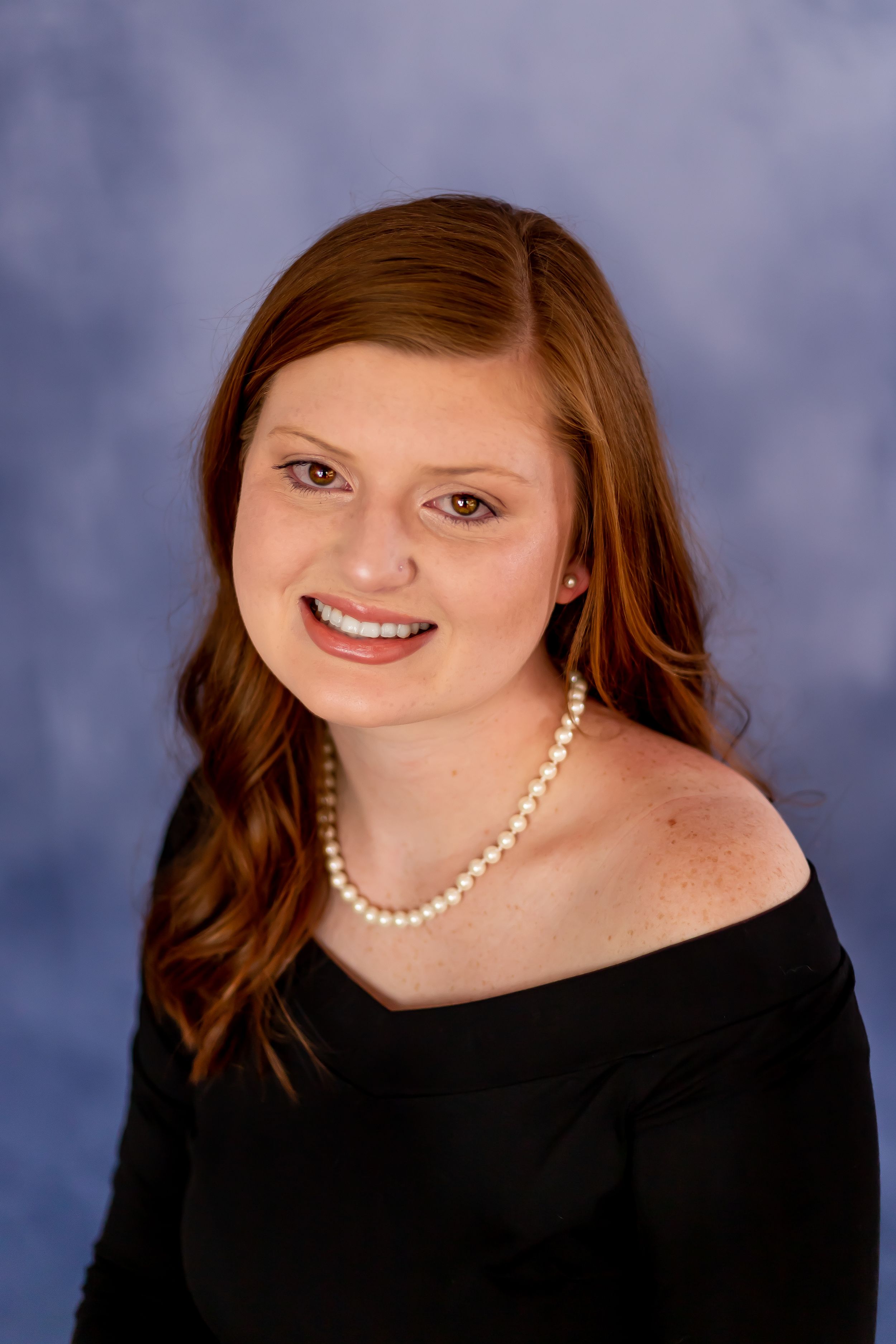 Studio portrait against blue background featuring black dress and pearl necklace.