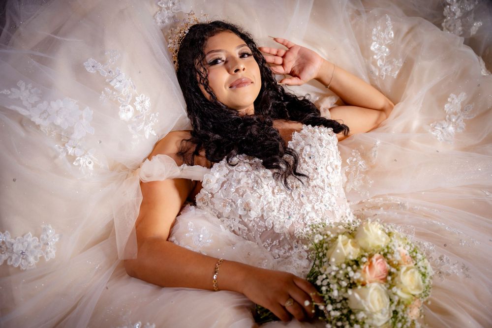 Bride in a white lace off-shoulder gown lying down holding a bouquet of white roses and baby's breath.