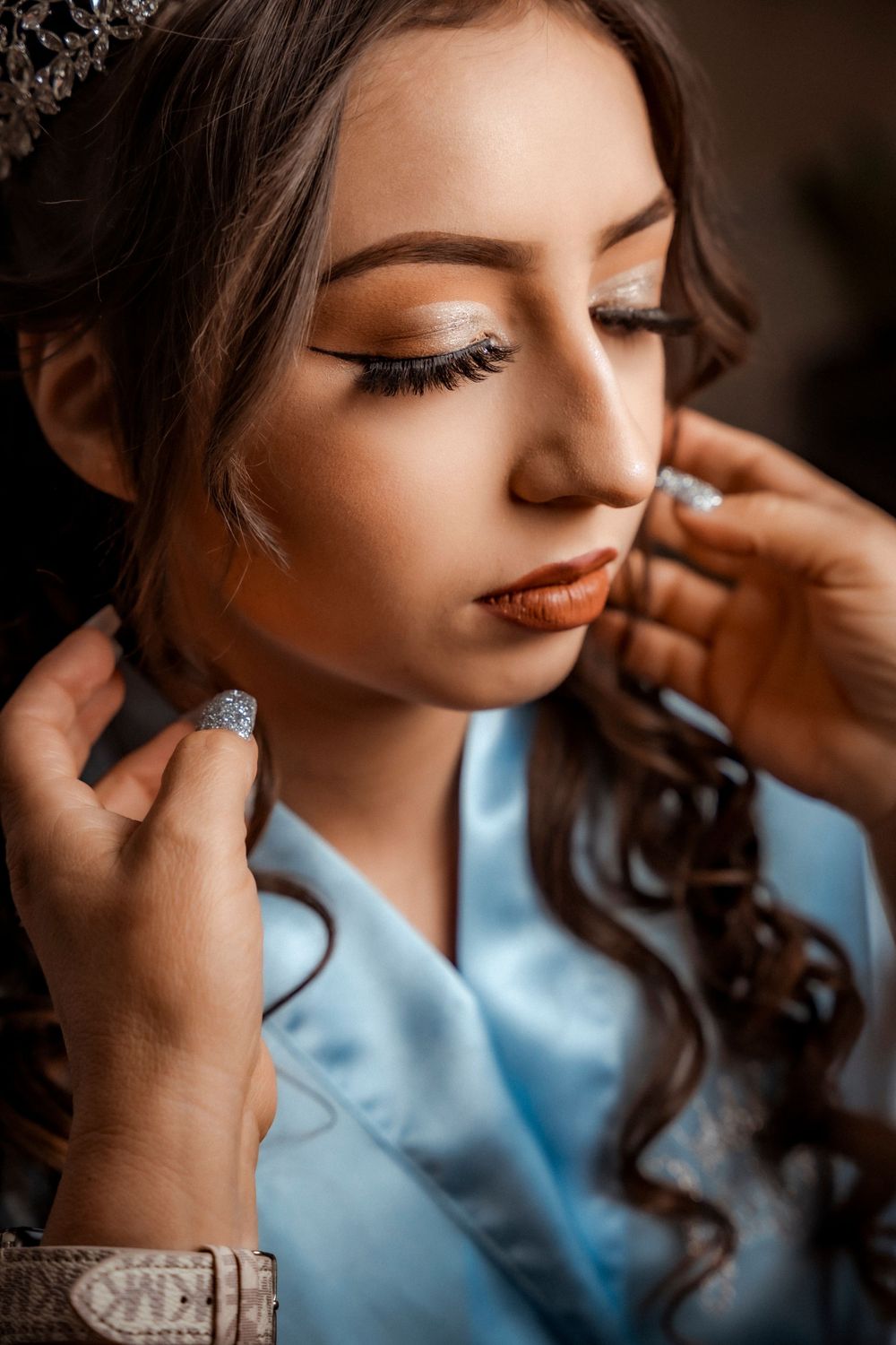 Close-up of a young woman with glamorous makeup and curly hair having diamond earrings put on.