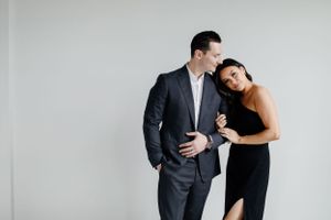Couple in formal attire embracing against white wall in studio setting.