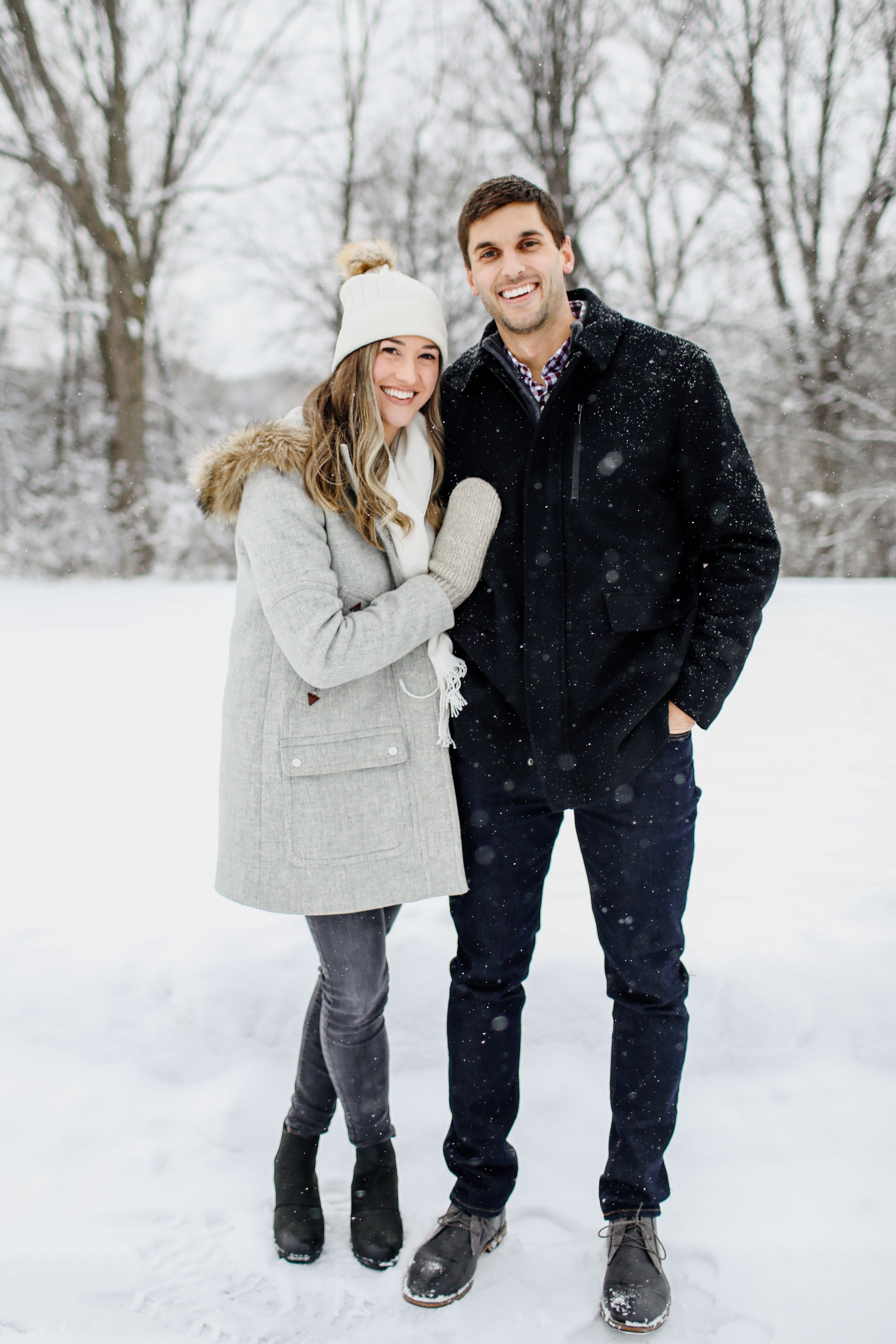 Couple playing in snow wearing winter coats during romantic photoshoot.