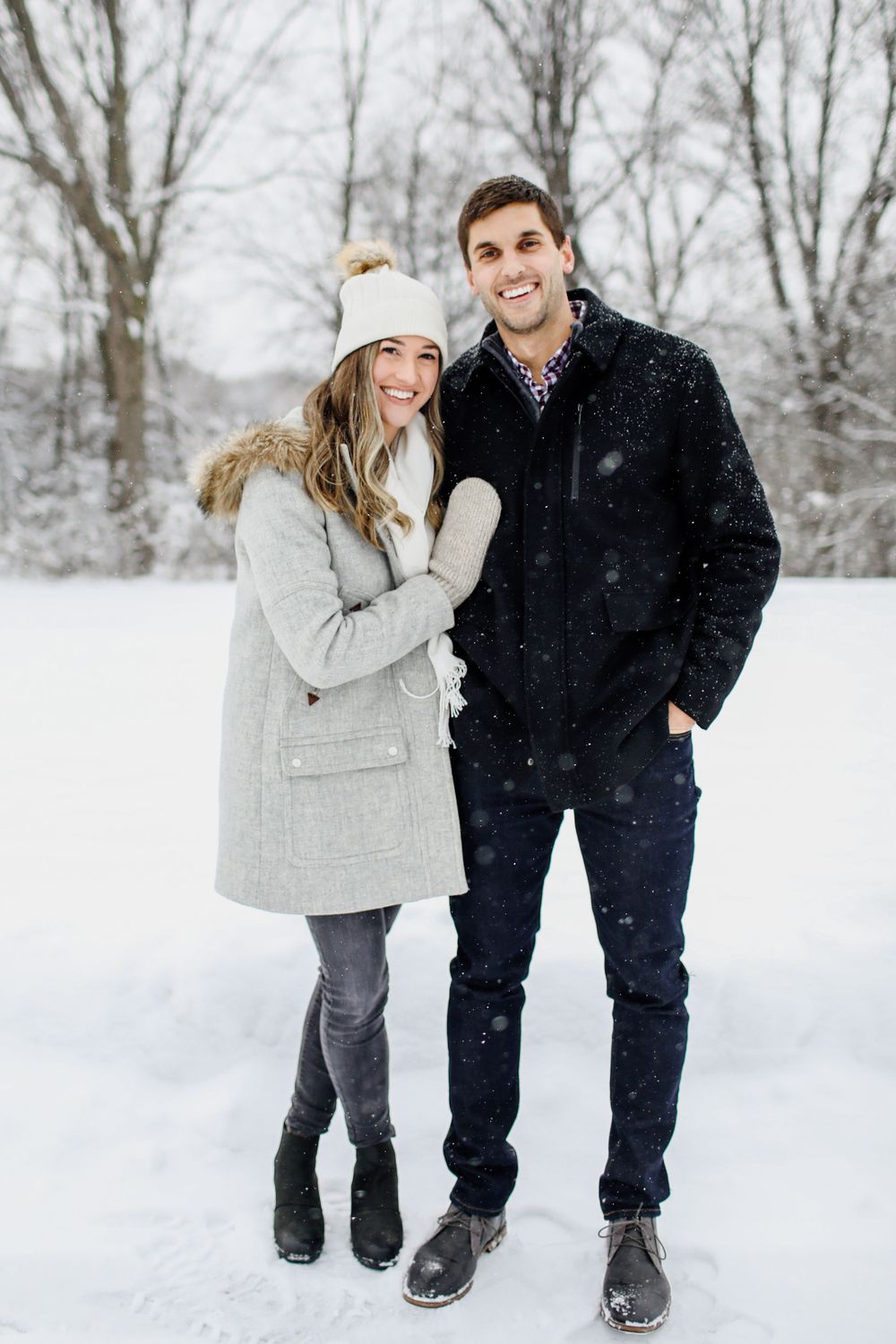 Couple playing in snow wearing winter coats during romantic photoshoot.