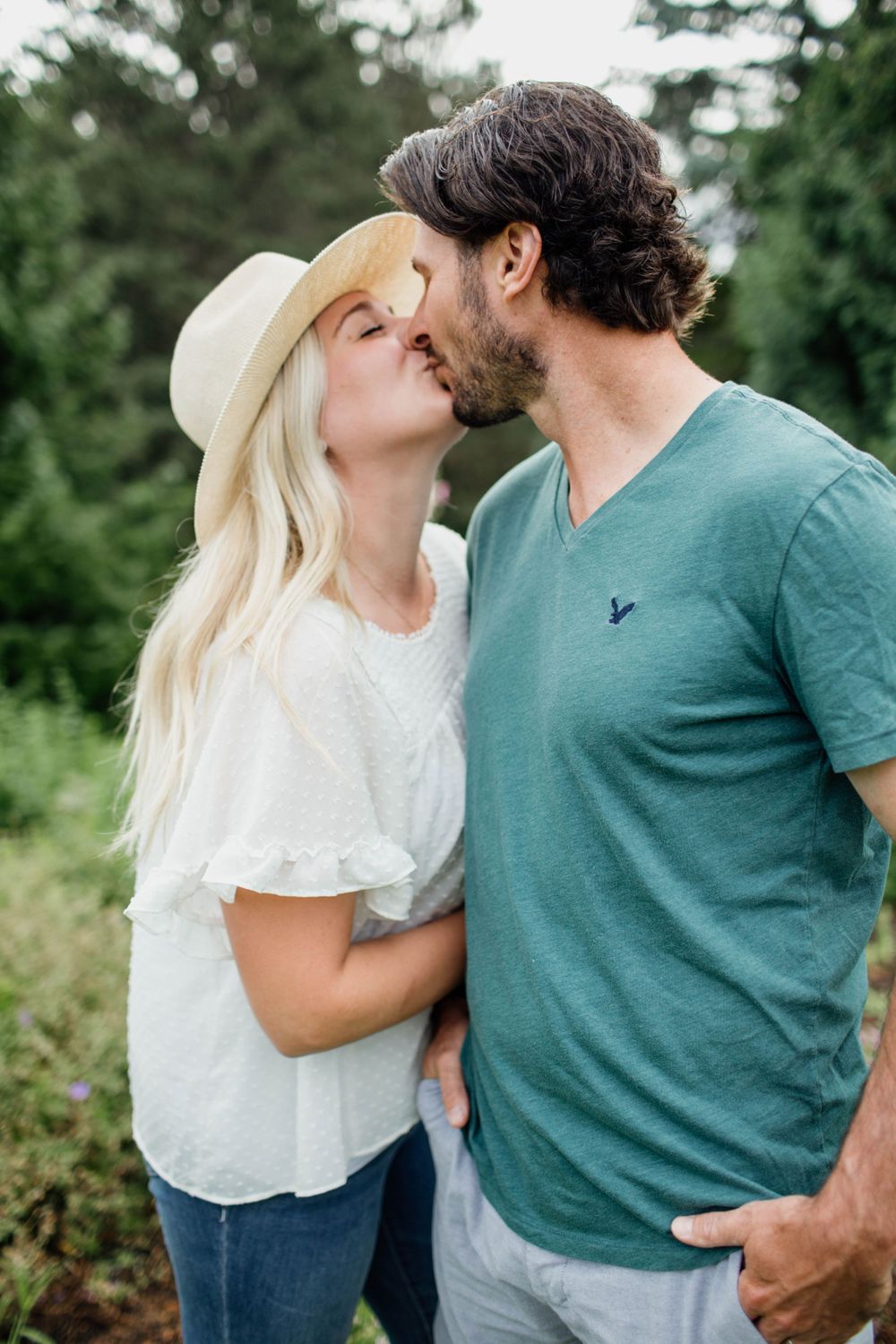 Romantic couple in casual attire sharing intimate moments in a natural outdoor setting with green foliage.