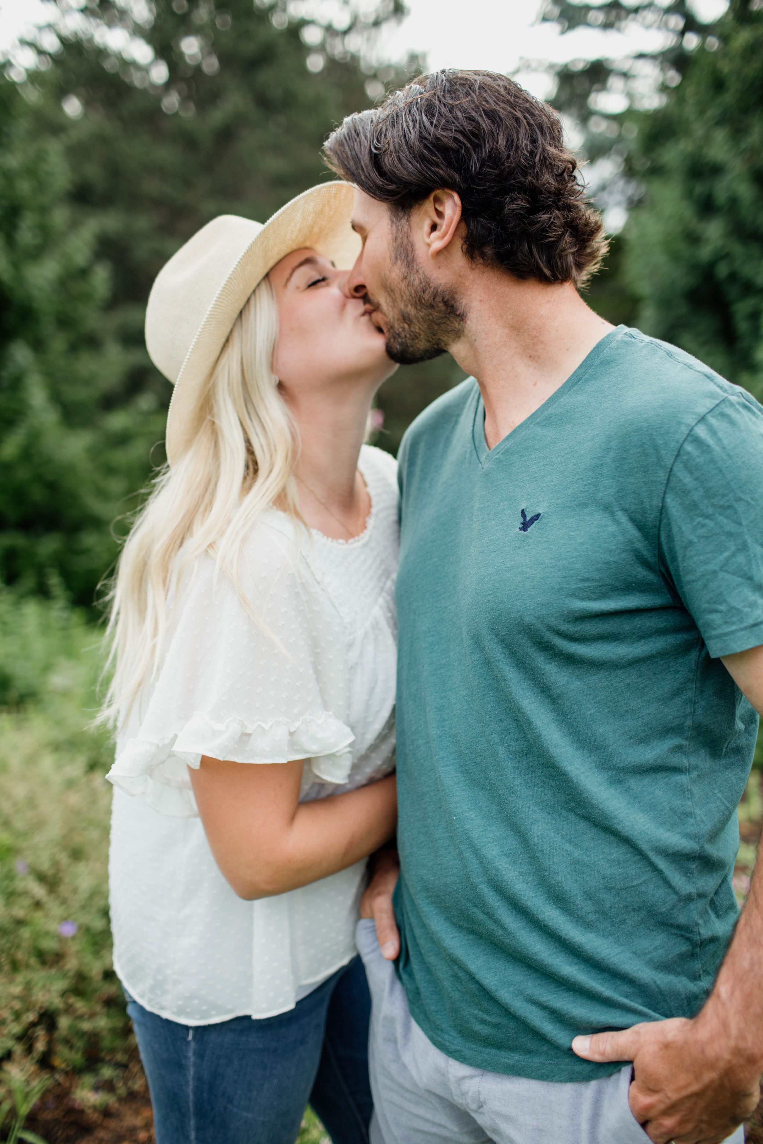 Romantic couple in casual attire sharing intimate moments in a natural outdoor setting with green foliage.