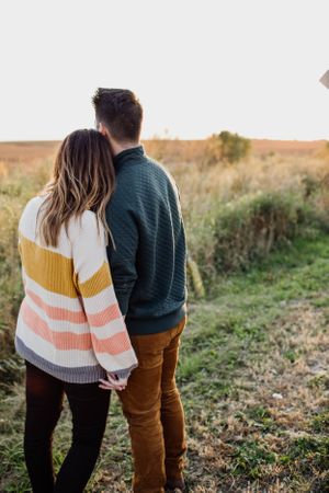 Couple in sweaters embracing in an autumn field at sunset.