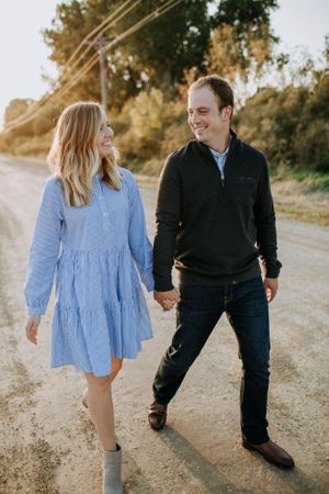 Couple walking together on a dirt path at sunset wearing blue dress and dark casual wear.