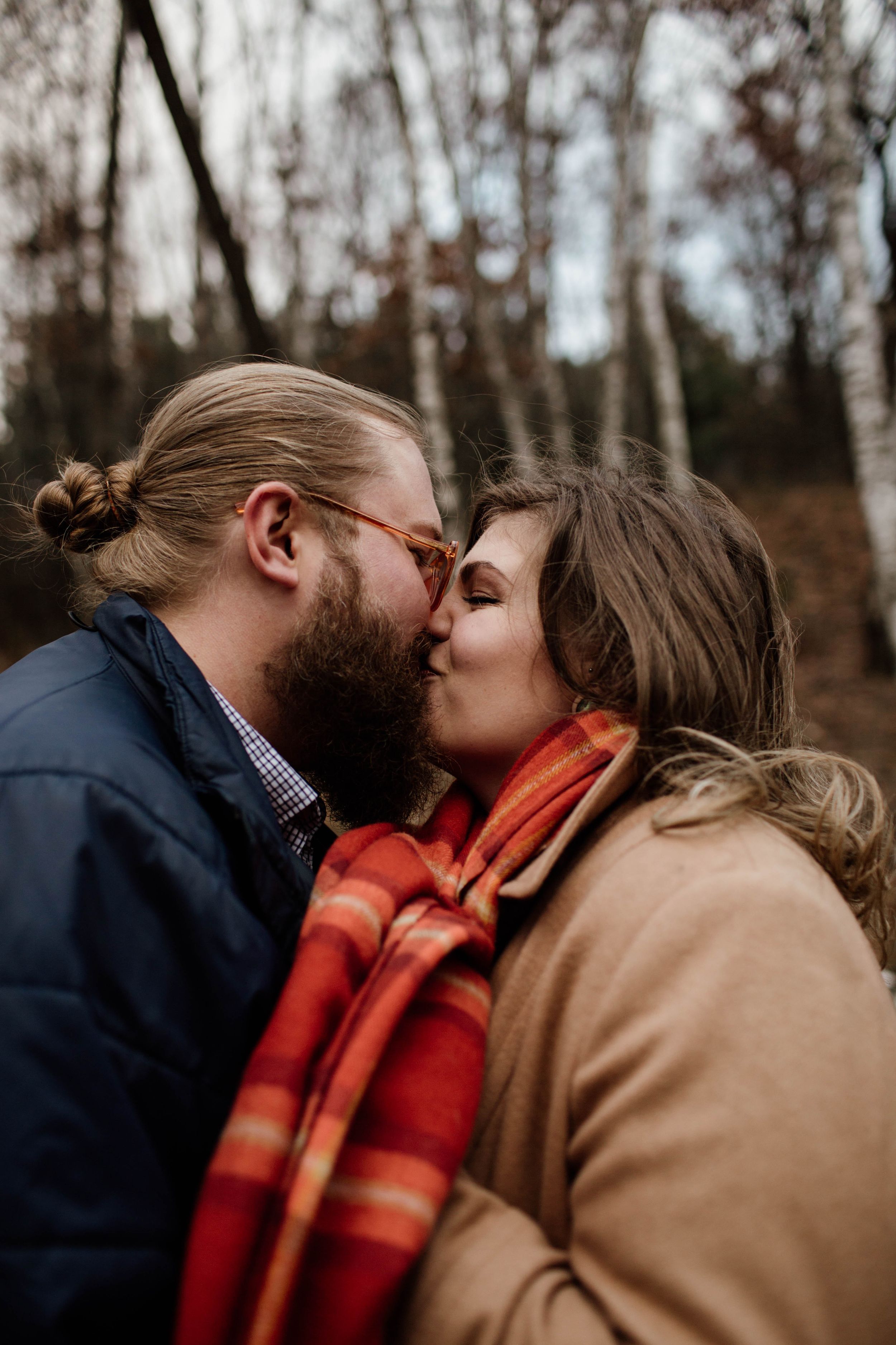 A cozy autumn scene with two people sharing an intimate moment wrapped in a red plaid scarf.