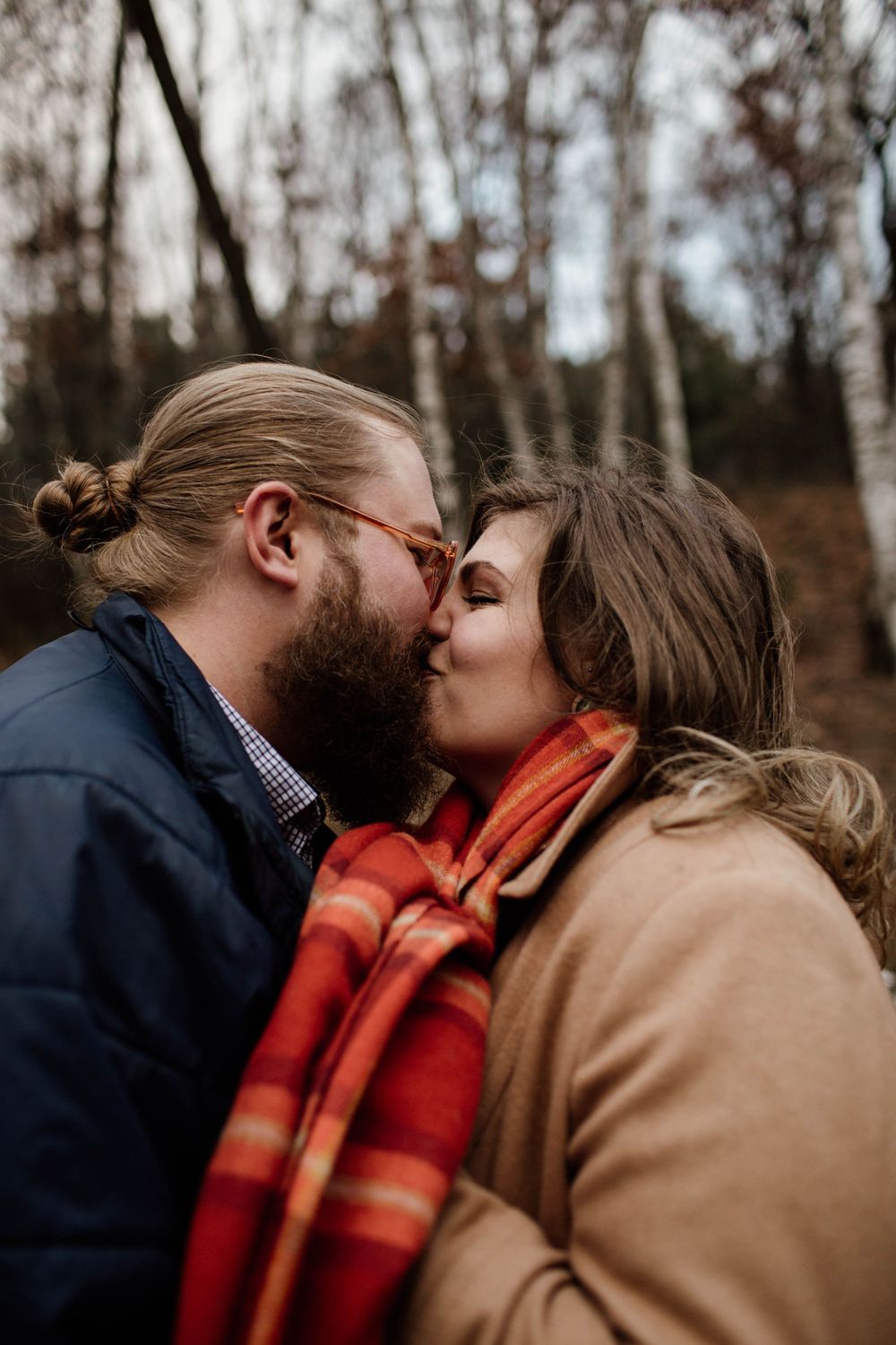 A cozy autumn scene with two people sharing an intimate moment wrapped in a red plaid scarf.